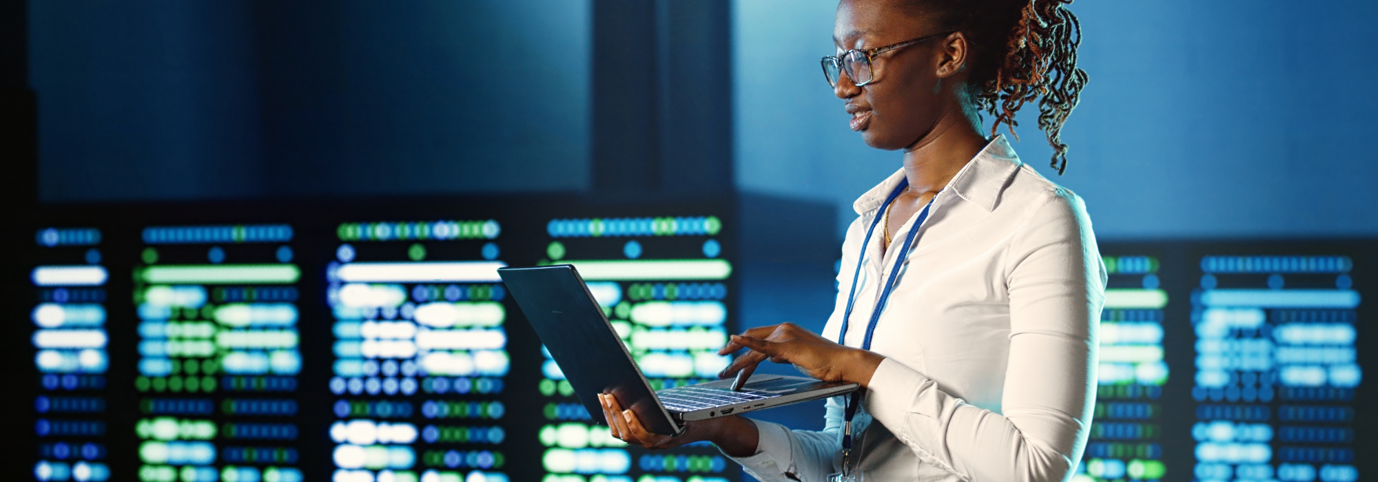 Cybersecurity analyst working in a security operations center (SOC), monitoring systems on a laptop against data center background.”